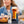 Smiling girl, blurry in the back, holding a clear image of a glass with nitro cold brew tea. She is sitting at a table with a bowl of oranges and berries. A can of East Forged black tea and yuzu with Mico smiling monkey is beside the glass