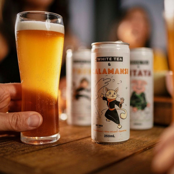 Hand holding a glass of nitro cold brew tea near the can with Saka cat on the front
